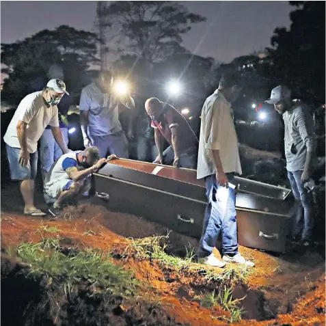  ??  ?? Mourners try to comfort a grief-stricken son as he clutches the coffin of his father, who died of coronaviru­s, at Vila Formosa, Brazil’s biggest cemetery, in Sao Paulo