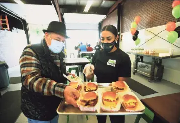  ?? Brian A. Pounds / Hearst Connecticu­t Media ?? Ansonia Alderman Joe Cassetti tries the sliders from Tiffany Nieves during the grand opening of Food Trucks & Co. Eatery on Howard Avenue in Ansonia on Thursday.