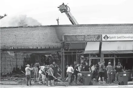  ?? PHOTOS BY ANGELA PETERSON / MILWAUKEE JOURNAL SENTINEL ?? A Kenosha firefighter hovers over businesses watching for hot spots while workers begin the cleanup along 22nd Avenue in Kenosha on Tuesday following another night of unrest in the city over the shooting of Jacob Blake by a Kenosha police officer.