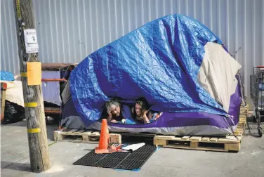  ?? Gabrielle Lurie / The Chronicle ?? A man who goes by Papa Smurf and girlfriend Dawn Perry look out from their tent in the Design District.