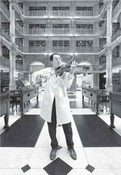  ?? AMY DAVIS/BALTIMORE SUN ?? Johns Hopkins neurologis­t Alex Pantelyat, co-founder and co-director of the Center for Music & Medicine, performs on the violin at the Peabody Library in Mount Vernon. The center’s goal is to integrate music and rhythm into medical care.