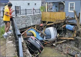  ?? AP/DAVID McFADDEN ?? Ellicott City, Md., residents gather on a bridge Monday to look at crumpled cars left by flooding of tributarie­s to the Patapsco River.