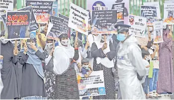  ?? — AFP file photo ?? A policeman stands guard as protesters hold placards during a demonstrat­ion against the government policy of forced cremations of Muslims who died of the Covid-19 coronaviru­s, outside a cemetery in Colombo.