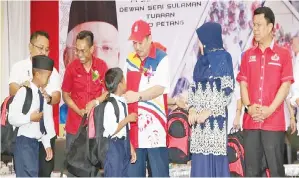  ??  ?? (Gambar atas) HAJIJI (tengah) dan Ahmad Fuad (dua kiri) membantu murid-murid memakai beg sekolah.