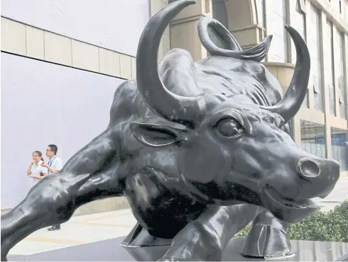  ?? REUTERS ?? People walk past a statue of a bull in front of an investment company in Beijing.