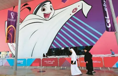  ?? MIGUEL MEDINA/GETTY-AFP ?? People make their way past a poster of the Qatar 2022 mascot La’eeb on Tuesday in Doha. Qatar is relocating Budweiser-branded beer stations at eight World Cup stadiums. Budweiser has been a fixture at World Cups since the 1980s.