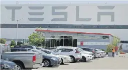  ??  ?? A masked man walks amid the nearly full parking lot at Tesla’s electric-car factory in Fremont, California, on Monday.