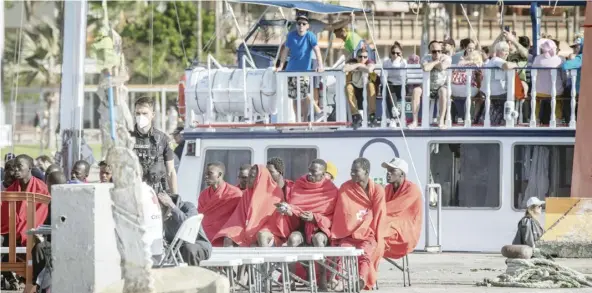  ?? DESIREE MARTIN/GENCE FRANCE-PRESSE ?? TOURISTS aboard a recreation­al boat look at 41 migrants sitting on the pier of Los Cristianos port following their rescue by the Spanish Salvamento Maritimo (Sea Search and Rescue agency) vessel ‘Salvamar Alpheratz’ off the coast of the Canary Island of Tenerife, Spain.