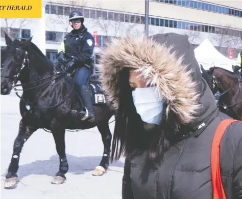  ?? PAUL CHIASSON/THE CANADIAN PRESS ?? A woman walks past mounted police outside a walk-in COVID-19 test clinic in Montreal on Wednesday. Many Canadians who have been tested for the virus have been kept in the dark about their results for days, as agencies have been overwhelme­d by the demand.