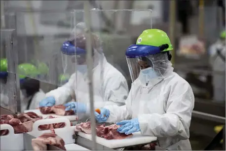  ??  ?? This May 20, 2020, photo provided by Smithfield Foods shows some of the measures the company says it has taken to limit the spread of the coronaviru­s inside its plants. Workers inside its Sioux Falls, South Dakota, pork processing plant wear protective gear and are separated by plastic partitions as they carve up meat. (Photo courtesy Smithfield Foods via AP)