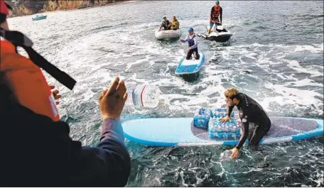  ?? Jay L. Clendenin Los Angeles Times ?? SURFERS HELP deliver cases of water to fire-afflicted Malibu residents Tuesday. A Good Samaritan had ferried the supplies by yacht.
