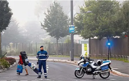  ?? — Reuters ?? Time to go: A woman carrying her belongings and walking past a police officer as people evacuate from a 1.5km radius around the Westend district in Frankfurt.