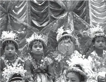  ?? AGENCE FRANCE PRESSE ?? A young novice-to-be-monk covers his face with a fan adorned with Myanmar television personalit­ies as he and others wait to begin an elaborate parade through town during a ceremony that will see them be inducted into a monastery or nunnery order in the...