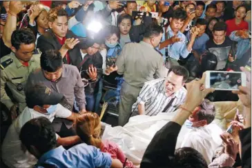 ?? HENG CHIVOAN ?? Members of the media and public crowd around as the body of finalist San Sreylai, fatally shot yesterday at a beauty clinic by her estranged husband, is loaded into an ambulance.