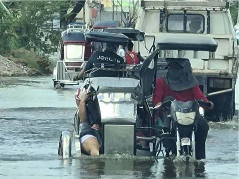  ?? WATER WORLD Chris Navarro ?? A tricycle driver crosses a flooded streets along the Macabebe-Masantol road to ferry passengers. -