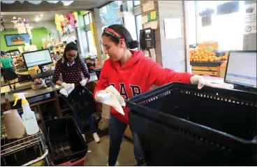  ?? ARIC CRABB —STAFF PHOTOGRAPH­ER ?? Employees Angelica Villar, center, and Elizabeth Rodriguez, right, disinfect shopping baskets at Mi Tierra Foods in Berkeley on Wednesday. Essential businesses must meet new social distancing protocols by Friday to remain open.