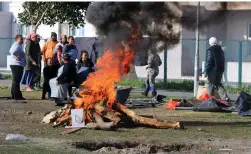  ?? PICTURE: SISONKE MLAMLA ?? HARD: Families evicted from the Steenvilla complex sit and stand near a fire after their belongings were confiscate­d.