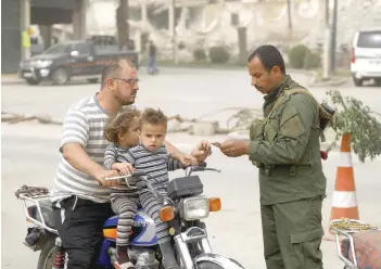  ?? — AFP ?? A member of the Raqa civil council’s local security forces checks the identifica­tion documents of a man riding a motorcycle at a checkpoint securing vehicles entering into the eastern Syrian city and former IS stronghold, on Wednesday.