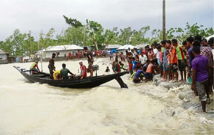  ?? — AP ?? Storm brewing: A boat bringing people to land as locals check an embankment before Cyclone Amphan made landfall in Shatkhira, Bangladesh.