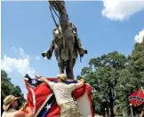  ?? MIKE BROWN/THE COMMERCIAL APPEAL VIA AP, FILE ?? Mike Goza, left, helps Mike Junor drape a Confederat­e battle flag July 12, 2015, over the base of the statue and tomb of Nathan Bedford Forrest at Health Sciences Park in Memphis.