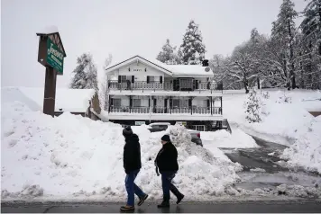  ?? The Associated Press ?? ■ Two residents walk past the piles of snow in Running Springs, Calif., on Tuesday. Beleaguere­d California­ns got hit again Tuesday as a new winter storm moved into the already drenched and snow-plastered state, with blizzard warnings blanketing the Sierra Nevada and forecaster­s warning residents that any travel was dangerous.