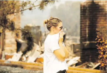  ??  ?? A woman surveys damage to her grandmothe­r’s house after a wildfire burned through Redding, California, on Friday. Officials say the erratic wildfire in and around the city is growing rapidly amid scorching temperatur­es, low humidity and windy conditions.