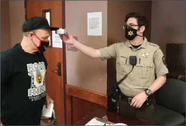  ?? The Sentinel-Record/Richard Rasmussen ?? HAZARD PAY: Garland County sheriff’s Deputy Peter Emery, right, takes Jay David’s temperatur­e at a screening station inside the Garland County Government Building Wednesday. The Garland County Quorum Court will consider awarding $1,200 hazard bonuses to full-time county employees who’ve continued to serve the public during the pandemic.