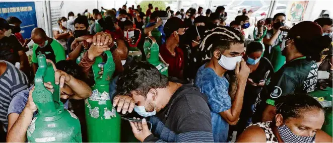  ?? Fotos Bruno Kelly/Reuters ?? Familiares de pacientes internados com ou sem Covid-19 seguram cilindros para serem abastecido­s por oxigênio hospitalar diante de fábrica em Manaus