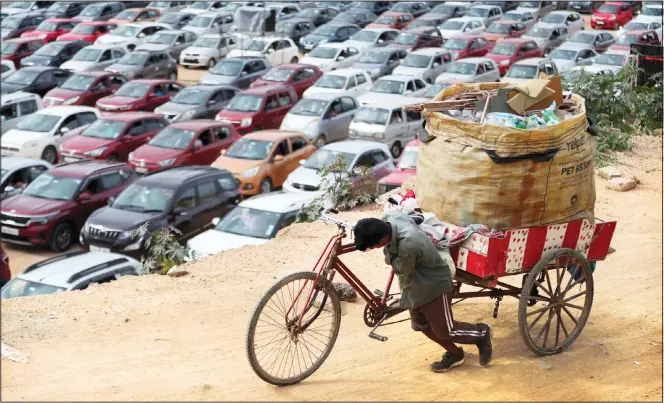  ??  ?? A ragpicker pushes his tricycle as Christians sit in their vehicles maintainin­g social distancing to prevent the spread of COVID-19 during a drive-in service at Bethel AG Church in Bengaluru, India on a recent Sunday. (AP)