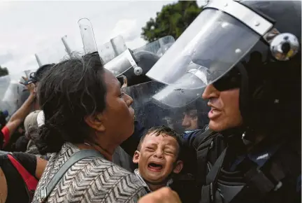  ?? Pedro Pardo / AFP / Getty Images ?? A Honduran migrant heading in a caravan to the United States, holds a crying baby while trying to cross the Guatemala-Mexico border bridge in Ciudad Hidalgo, Chiapas state, Mexico. Mexico deployed more police to its border, and Secretary of State Mike Pompeo met with Mexican officials about heading off the thousands of migrants before they reach the United States. Mexico asked the United Nations to set up a processing center, a plan Pompeo welcomed. “We are quickly reaching a point which appears to be a moment of crisis,” Pompeo said.