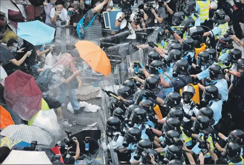  ?? ASSOCIATED PRESS ?? VINCENT YU Riot police use pepper spray on protesters after thousands blocked a road in Hong Kong’s financial district and government headquarte­rs. The people used umbrellas and plastic wrap to combat the spray yesterday.