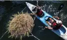  ?? Photograph: Boston Globe/ Getty Images ?? In a kayak, Louiza Wise, left, and Tyler McCormack work to tie down the ‘Emerald Tutu’, a floating swampland being deployed in East Boston.