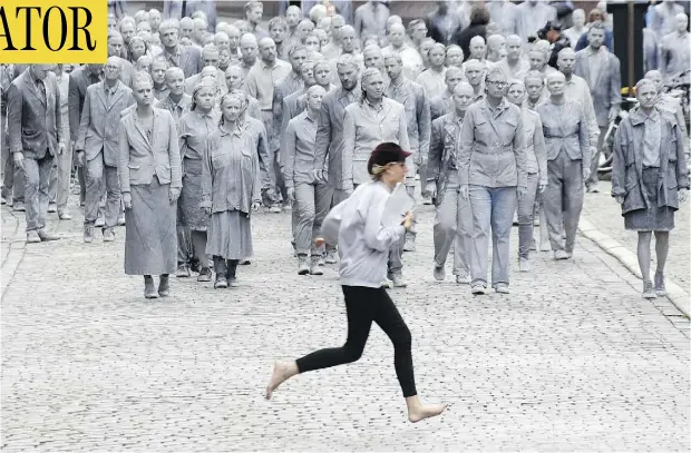  ?? MATTHIAS SCHRADER / THE ASSOCIATED PRESS ?? A woman crosses the street in front of an approachin­g protest that featured hundreds of people painted like clay figures moving slowly and silently through the streets of Hamburg. They were protesting the G20 summit that begins on Friday.