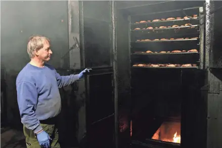  ?? TODAY NETWORK-WISCONSIN ?? Paul LeClair, president of Susie-Q Fish Market, checks over one of his smoker units this month in Two Rivers. LeClair says that smoked fish is more popular during the Lenten season. Maple wood is used for the fire in the smoker.