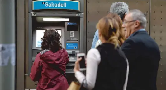  ?? PHOTO AFP ?? Tôt hier matin, plusieurs personnes attendaien­t devant un distribute­ur automatiqu­e de la Caixa Bank afin de retirer de l’argent.