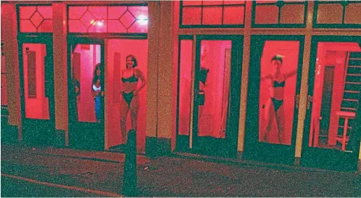  ?? AP ?? Prostitute­s stand behind red-lit windows, waiting for customers in Amsterdam’s Red Light district. The city’s new mayor has presented options for improving conditions for sex workers, cutting crime and reducing the burden of mass tourism in the area.
