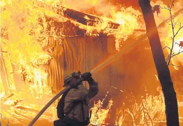  ??  ?? MORE FIRES IN THE FUTURE: A firefighte­r fights a blaze at a residence in California earlier this month. The findings of a report issued on Friday cited increasing water scarcity in dry regions, torrential downpours in wet regions and more severe heat waves and wildfires.