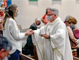  ?? Photos by Ronald Cortes / Contributo­r ?? Father Pat O'brien distribute­s communion to Molly Pe and others at St. Pius X Catholic Church. The wearing of masks during services there is encouraged but not mandatory.