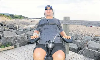  ?? CAPE BRETON POST ?? Callum MacQuarrie sits in his motorized wheelchair on the boardwalk at Inverness beach on Tuesday. In the background is the breakwater where he broke his neck diving into the shallow water below 23 years ago. MacQuarrie, who is co-chair of the...