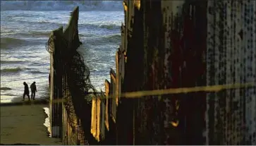  ?? Gregory Bull Associated Press ?? A TRANSITION in power has rarely represente­d such a sharp contrast in approaches to immigratio­n and border security. Above, two men walk where border fencing meets the Pacific Ocean last month in Tijuana.