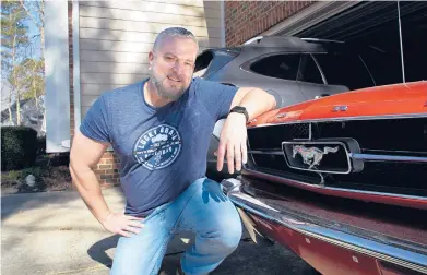  ?? ALLEN G. BREED/AP ?? Steve Bock kneels beside his 1965 Ford Mustang at his home in Apex, North Carolina. He recently bought a Subaru Outback, but would like to have an electric or hybrid car if they were cheaper. Electric vehicles make up less than 2% of new vehicle sales in the U.S.