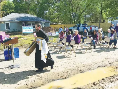  ?? Staff photo by Greg Bischof ?? ■ The Rev. Justin Braun of Sacred Heart Catholic Church walks along Redwater’s Church Street to participat­e in the Home Blessing Dedication of the first Habitat For Humanity home built in the city. Braun delivered the ceremony’s opening prayer.