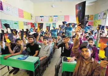  ?? AP ?? Catching them young Pakistani students raise copies of comic books after their teacher handed out the books regarding counterter­rorism distribute­d by a nongovernm­ent organisati­on run by Gauher Aftab at a school in Lahore, Pakistan.