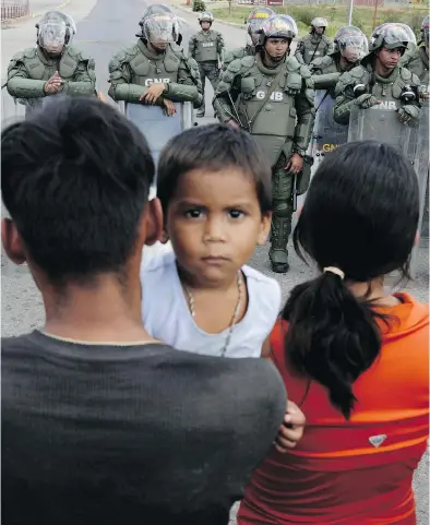  ?? RICARDO MORAES / REUTERS ?? People waiting to cross to Venezuela stand opposite Venezuelan national guards at the border in Pacaraima, Roraima state, Brazil, on Friday. Venezuelan President Nicolas Maduro has ordered the border closed.