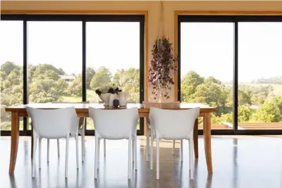  ??  ?? The centrally placed dining table floats between two walls of black sliding doors which frame the views on both sides of the home.