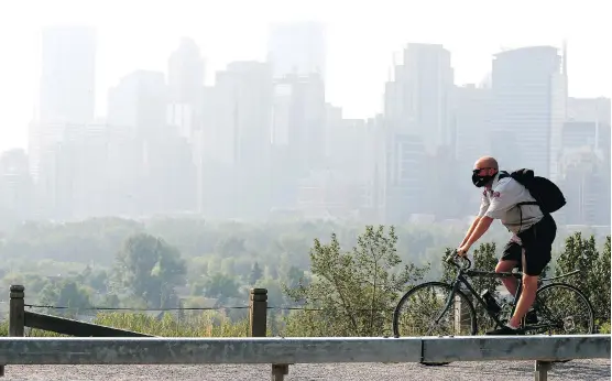  ?? DARREN MAKOWICHUK ?? Jerry Hoult of Canada Post rides past the smoky city skyline on Wednesday. Air quality is expected to worsen before the weekend.