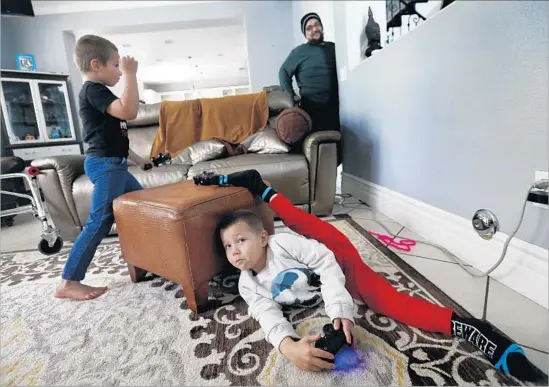  ?? Photograph­s by Mel Melcon Los Angeles Times ?? LUCIAN OLIVERA, center, stretches his legs in March. His brother Nikolas is at left and their father, Israel, at right. Lucian and other children like him suffer from acute f laccid myelitis, which alarms and puzzles scientists. This kind of sudden and...