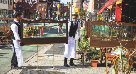  ?? Reuters ?? Waiters adjust social distancing screens outside for outdoor seating that follows current health guidelines to slow the spread of coronaviru­s at a restaurant in New York City on Wednesday.