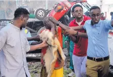  ?? FARAH ABDI WARSAMEH/ASSOCIATED PRESS ?? Somalis help a wounded man who was injured when a truck bomb exploded outside a popular hotel in Somalia’s capital of Mogadishu Saturday. At least 23 people died in the attack.