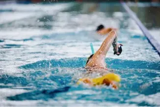  ??  ?? Das Training mit Paddles (Handflosse­n) und Pullbouy (eine Art Boje für die Beine) sollen Elenas Körperhalt­ung im Wasser verbessern